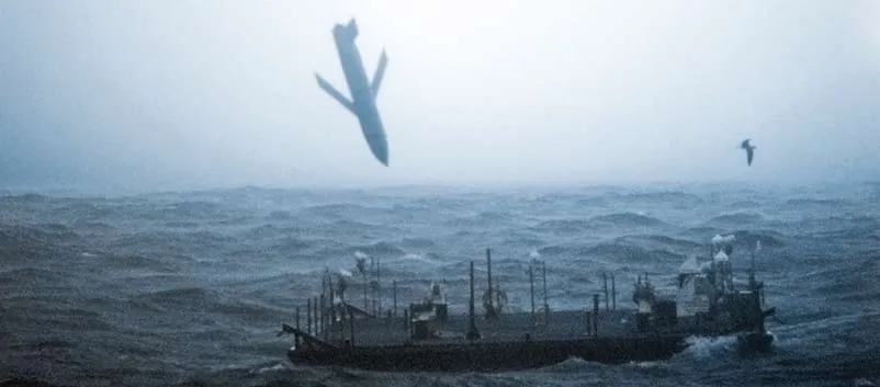 A Joint Air to Surface Standoff Missile falls toward the sea beside a small floating target platform in grey, rough water, with a gull in the air to the right.