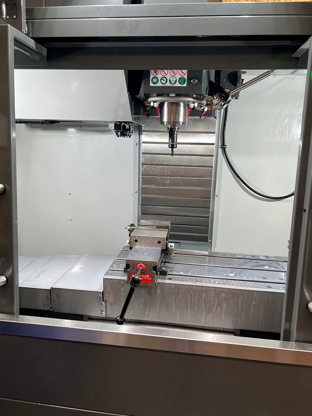 Inside the enclosure of a vertical mill: the spindle above a vise clamped to the machine table