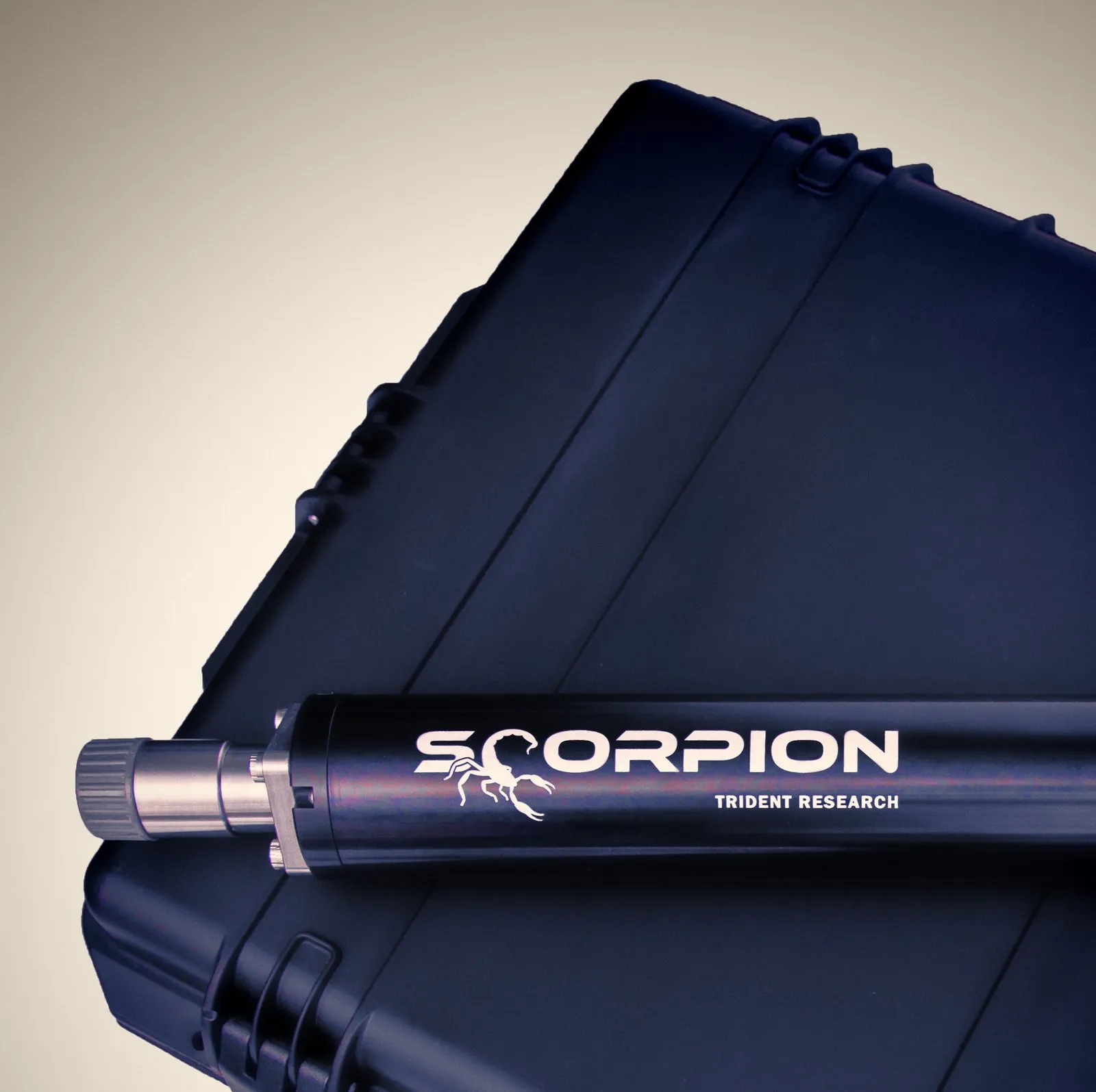 A close view of the black Scorpion sparker, its steel end fitting and knurled cap pointing left, with white SCORPION lettering, a scorpion emblem and TRIDENT RESEARCH along the tube, lying on a navy hard case against a grey-brown backdrop