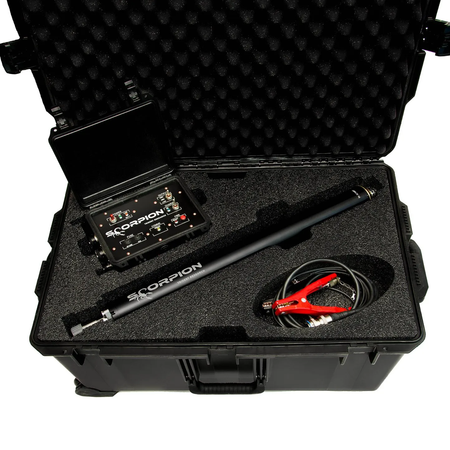 A black wheeled hard case opened from above: in grey foam, a control unit with its own lid raised at upper left, the black Scorpion sparker tube lying diagonally across the middle, and a coil of lead with red battery clamps at lower right